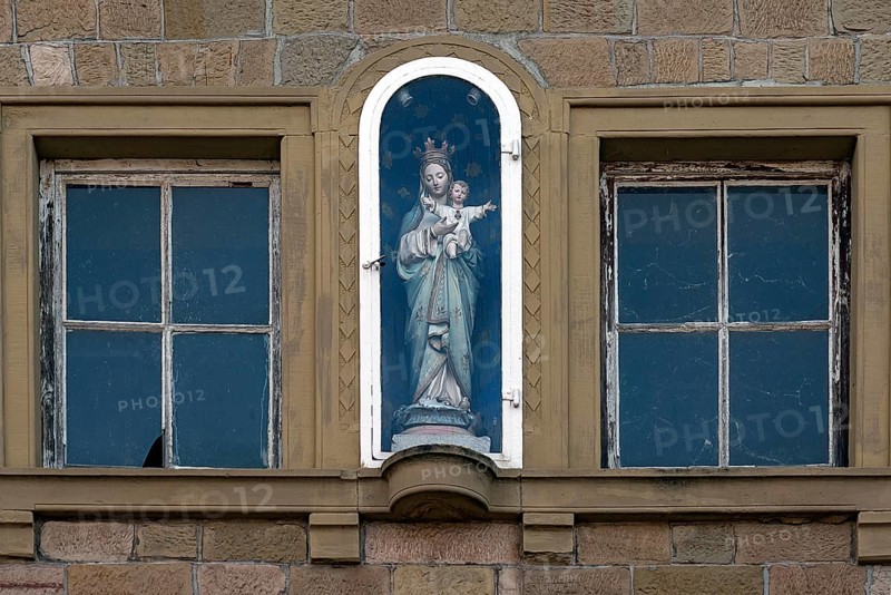 Figure of a saint on a house facade in a niche behind glass