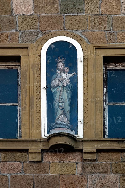 Figure of a saint on a house facade in a niche behind glass
