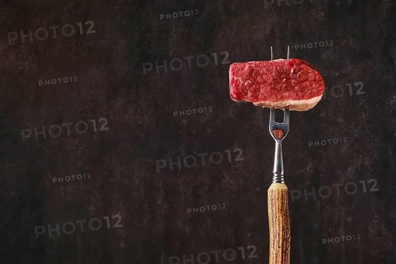 Raw beef brisket flat steak on fork with place for text