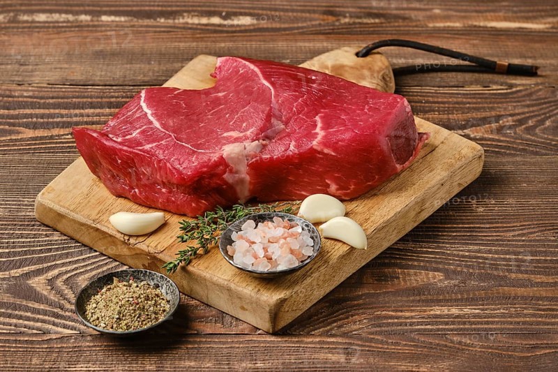 Fresh raw top side beef steak on wooden cutting board ready for barbeque