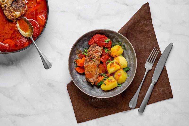 Slow cooking food. Stewed bottom round roast beef meat in beer gravy with tomatoes and carrot