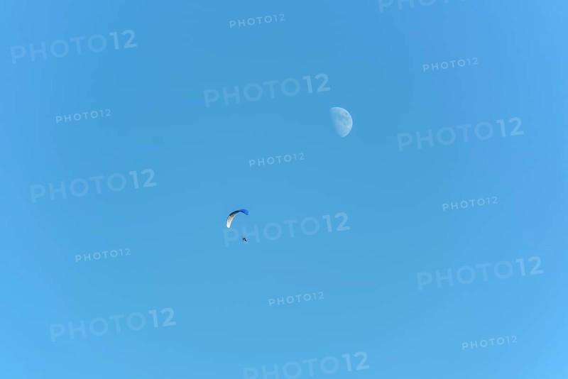 Paramotor in flight on a sunny day with the moon in the sky. France