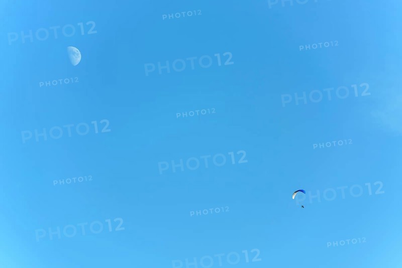 Paramotor in flight on a sunny day with the moon in the sky. France