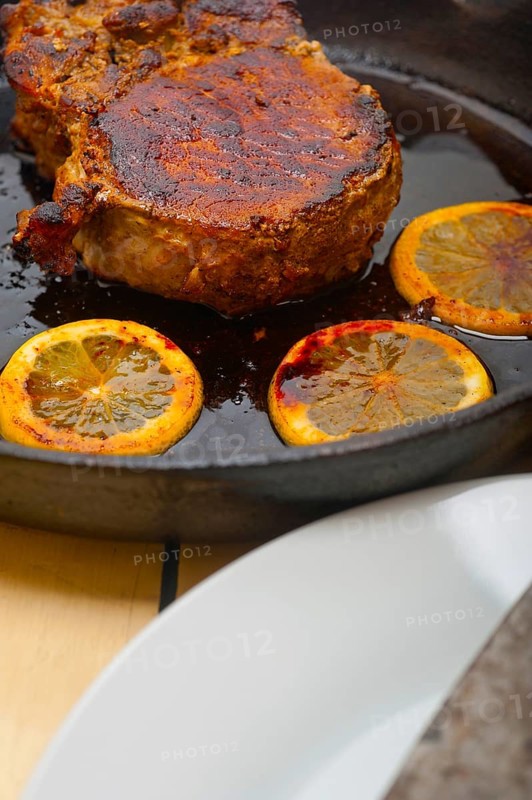 Pork chop seared on iron skillet with lemon and spices seasoning