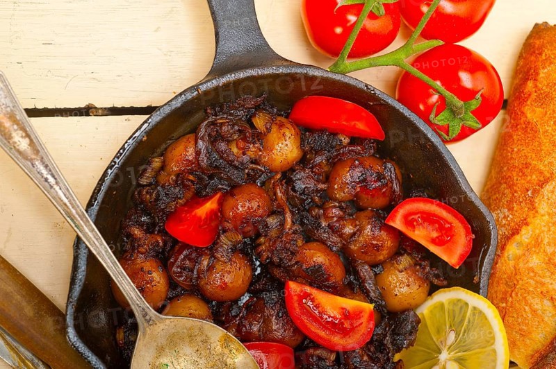 Baby cuttle fish roasted on iron skillet with tomatoes and onions over rustic wood table