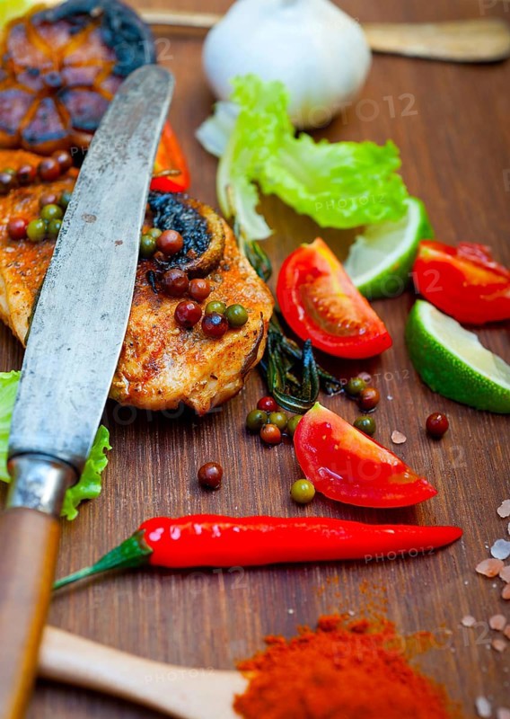 Wood fired hoven cooked chicken breast on wood board with herbs spices and vegetables