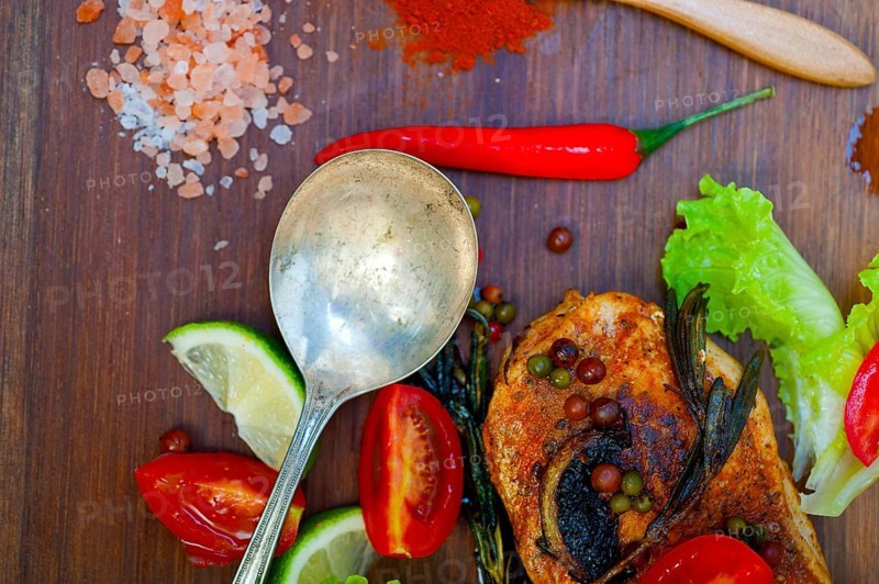 Wood fired hoven cooked chicken breast on wood board with herbs spices and vegetables