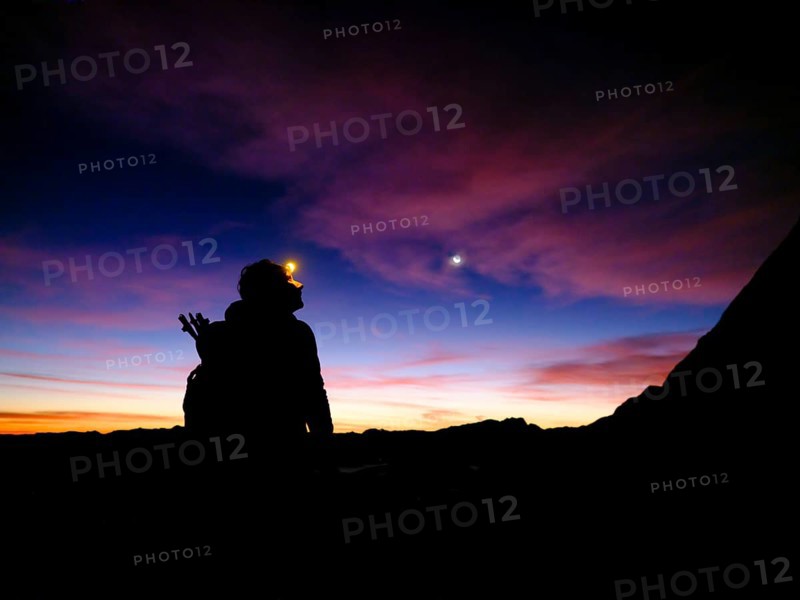 Silhouette of a female mountaineer with headlamp at dawn