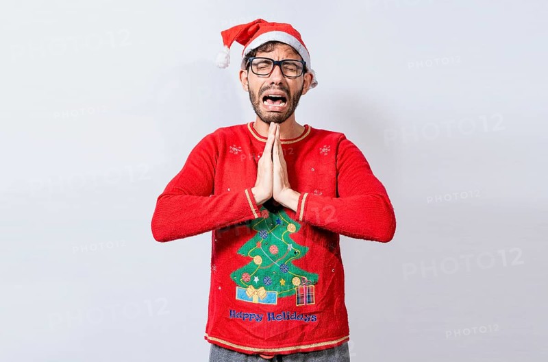 Man with christmas hat with hands together in pleading gesture. Christmas guy with hands together begging for a Christmas wish