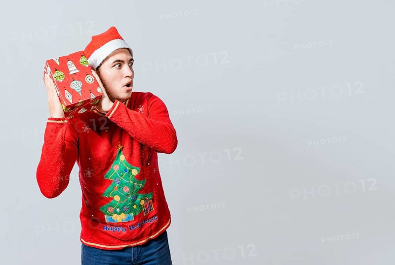 Christmas guy holding and listening a gift box. Excited christmas people holding and listening a gift. Concept of guessing a christmas gift
