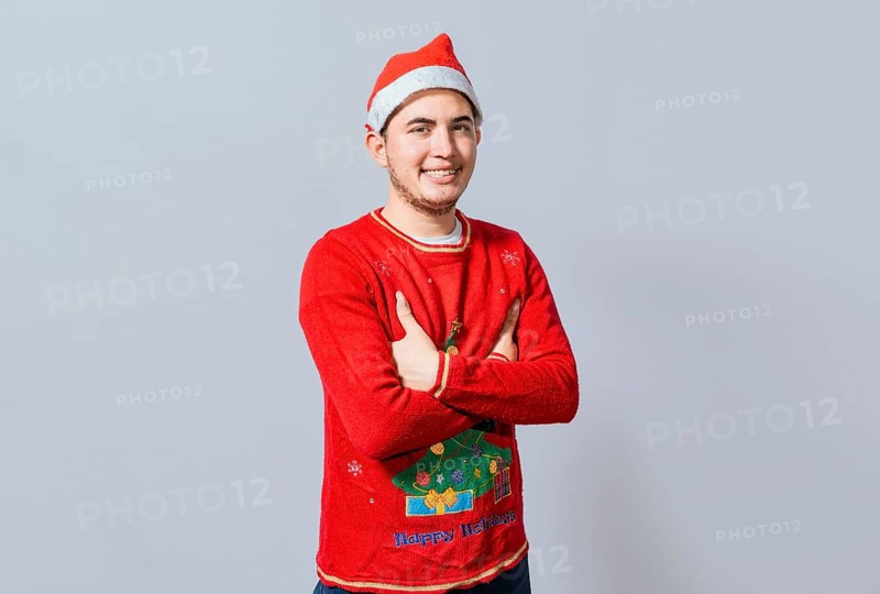 Portrait of guy in sweater and christmas hat with crossed arms isolated. Smiling guy in christmas hat with crossed arms smiling. Teenage guy in christmas clothes with crossed arms smiling