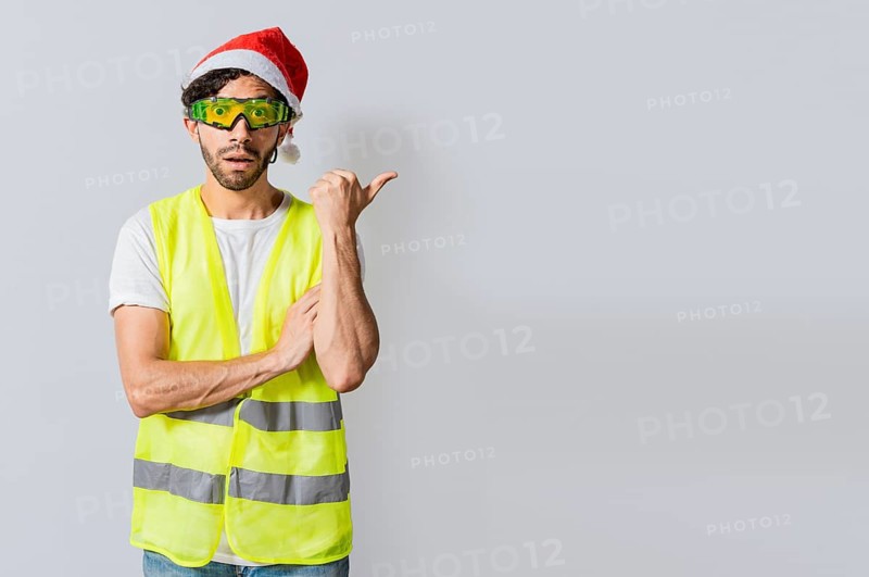 Amazed builder engineer in christmas hat pointing a copy space. Engineer man in christmas hat showing a product
