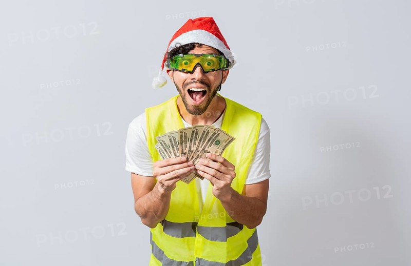 Engineer in christmas hat holding money smiling at camera. builder engineer in christmas hat with happy expression holding dollars isolated. Concept of engineer with money in holiday season