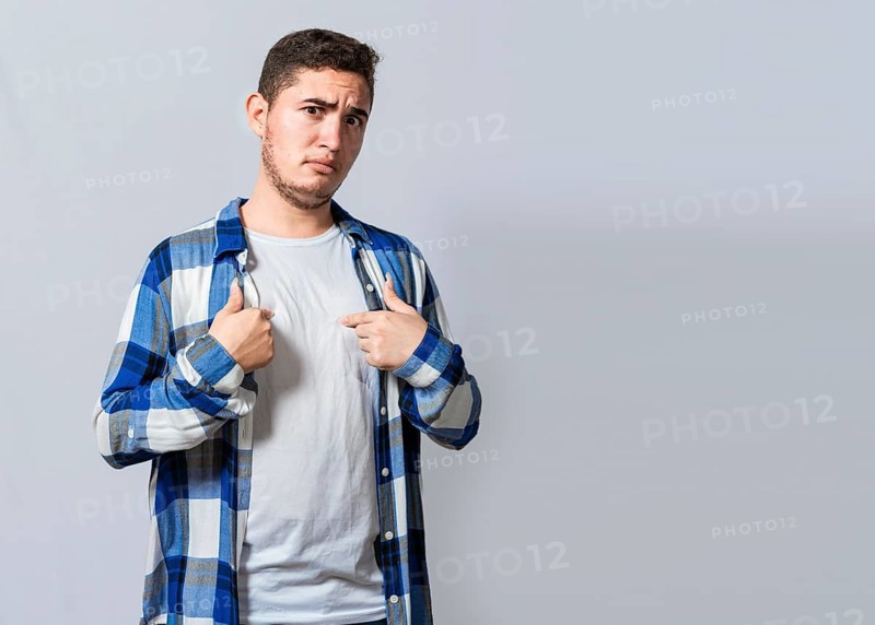 Confused caucasian young man pointing at himself. Confused person pointing at himself isolated. Confused latin guy pointing at himself isolated