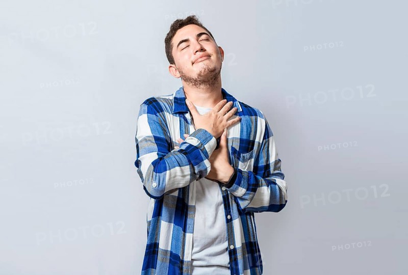 Grateful young guy smiling with hands on chest