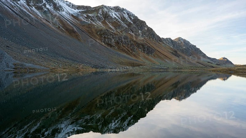 Slightly snow-covered mountains reflected in Lake Schotten in autumn at the Flueela Pass