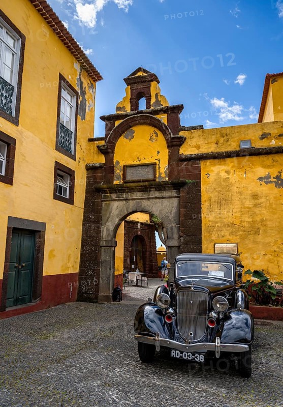 Vintage car parked in front of yellow gate and wall