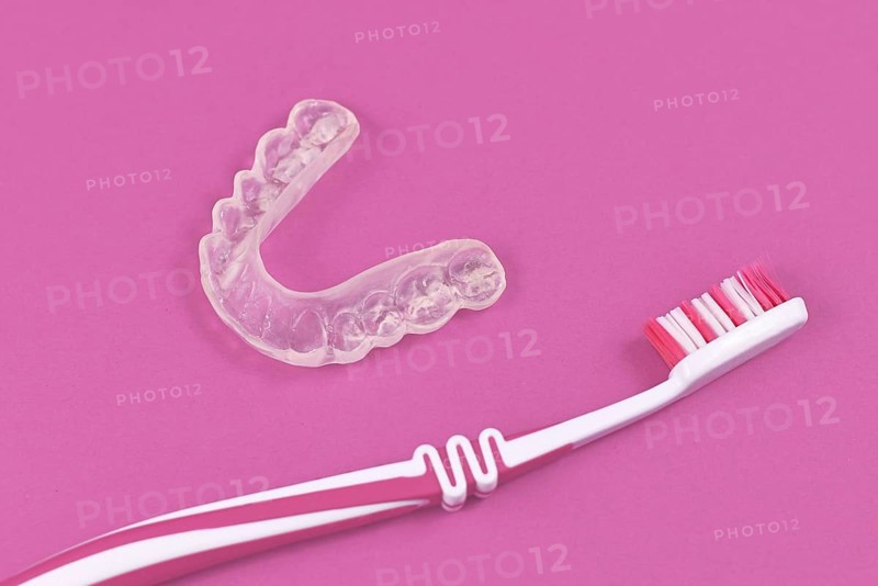 Customized transparent teeth bite guard clear aligners for lower jaw with tooth brush on pink background
