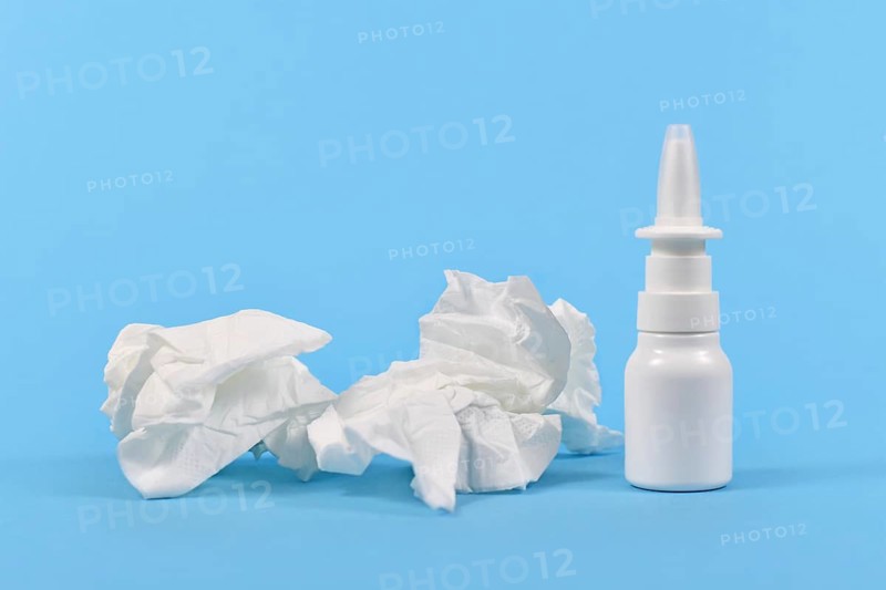 Nasal spray bottle and used tissues used during common cold on blue background