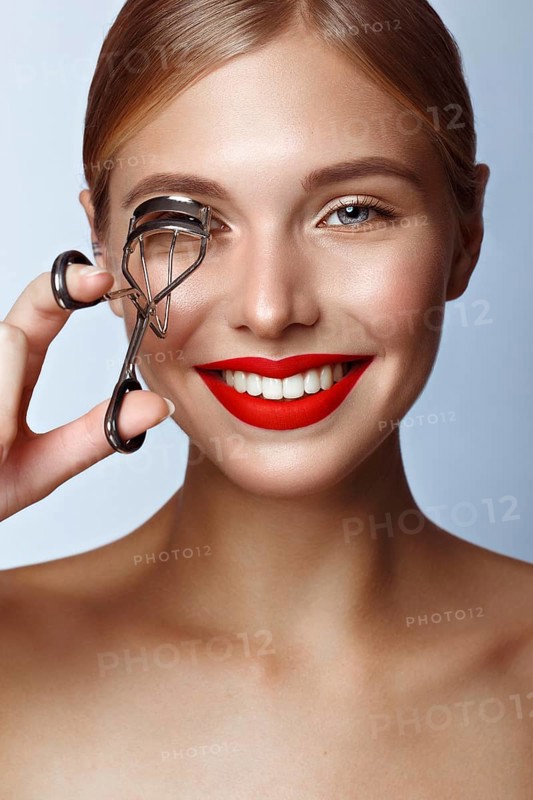 Beautiful girl with red lips and classic makeup with curler in hand. Beauty face. Photo taken in the studio