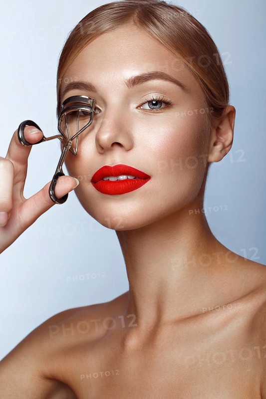 Beautiful girl with red lips and classic makeup with curler in hand. Beauty face. Photo taken in the studio