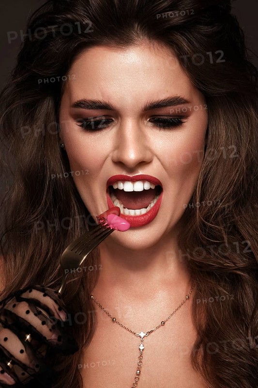 Beautiful girl with red lips and classic makeup and curls with lipstick in hand. Beauty face. Photo taken in the studio
