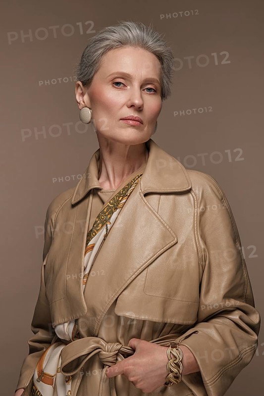 Portrait of a beautiful elderly woman in a beige raincoat with classic makeup and gray hair
