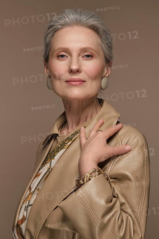 Portrait of a beautiful elderly woman in a beige raincoat with classic makeup and gray hair