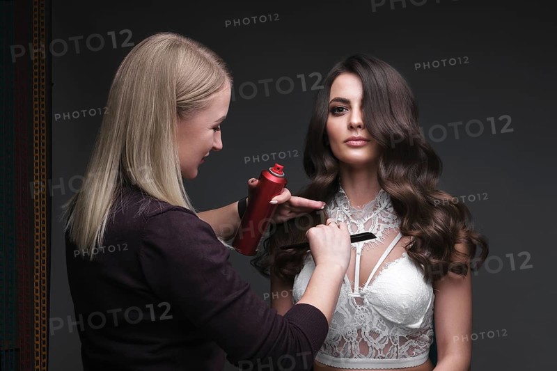 Hairdresser and beautiful brunette girl with a perfectly curls hair and classic make-up. Beauty face. Picture taken in the studio