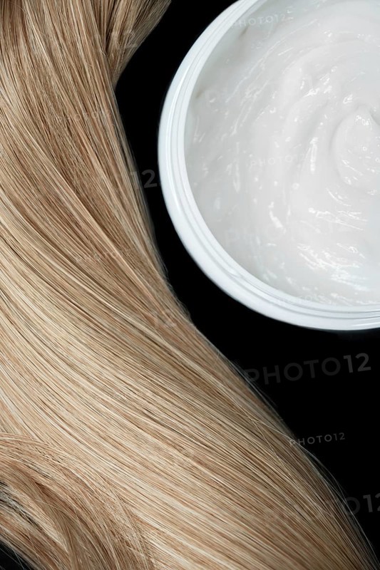 A strand of blond hair with hair balm on a black background. Close-up