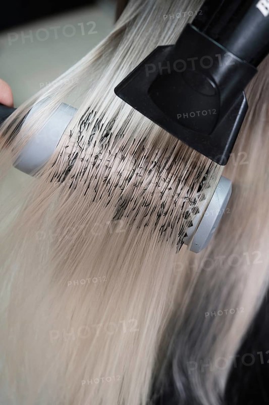 Young woman in a hairdressing salon dyes her hair blond and dries hair