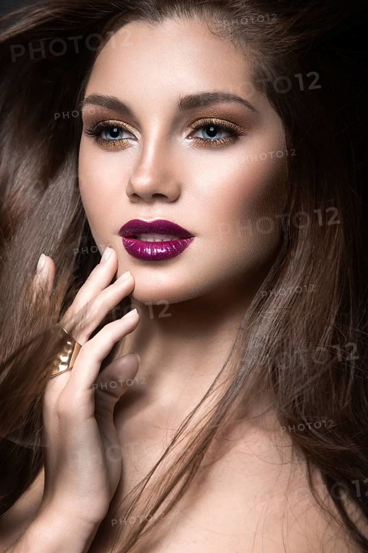 Beautiful girl with golden makeup and burgundy lips with the wind in hair. Beauty face. Picture taken in the studio on a black background