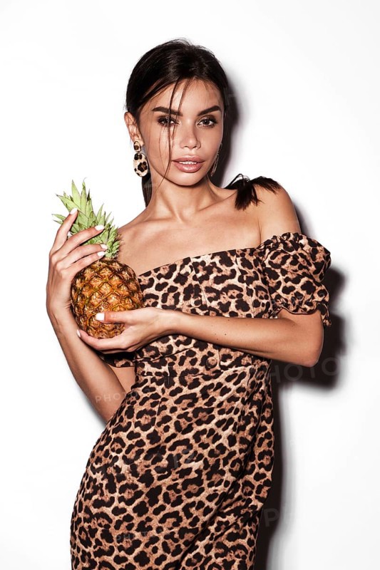 Beautiful sexy woman with pineapple in hands in a leopard dress and earrings