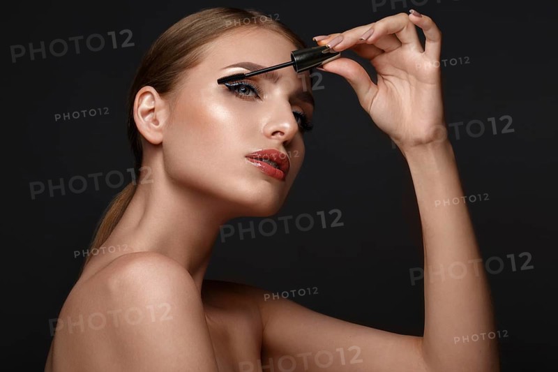 Beautiful girl with sexy lips and classic makeup with cosmetic mascara brush in hand. Beauty face. Photo taken in the studio