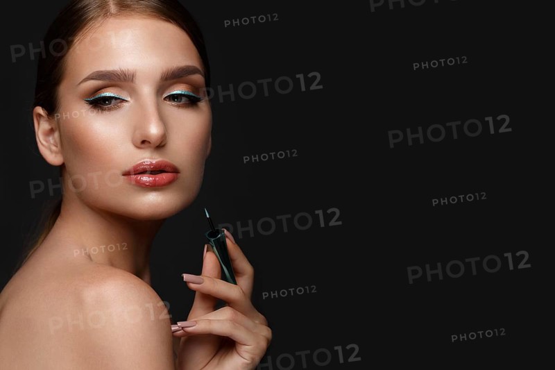 Beautiful girl with sexy lips and classic makeup with cosmetic blue eyeliner in hand. Beauty face. Photo taken in the studio
