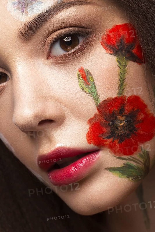 Beautiful brunette girl with curls and a floral pattern on the face. Beauty flowers. Portrait shot in studio