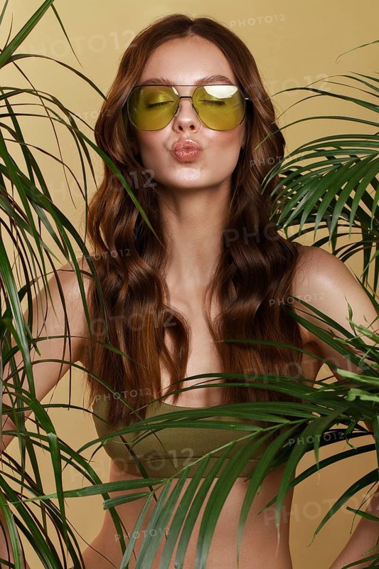 Beautiful sexy woman in a bikini posing in the middle of green plants. Summer look. Beauty face. Photo taken in the studio