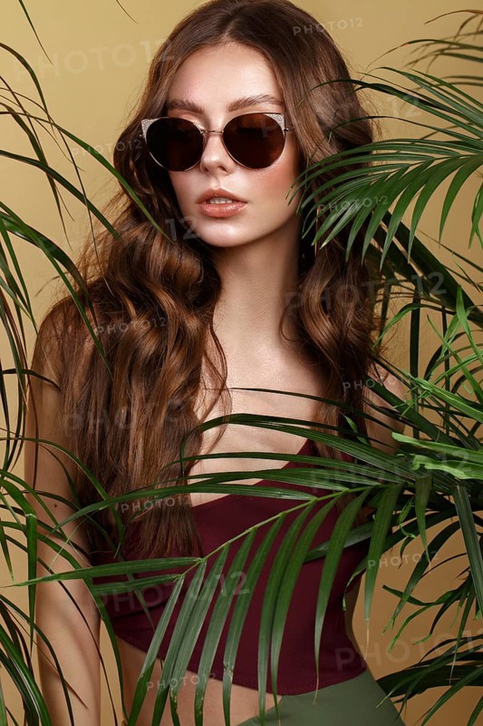 Beautiful sexy woman in a bikini and sunglasses posing in the middle of green plants. Summer look. Beauty face. Photo taken in the studio