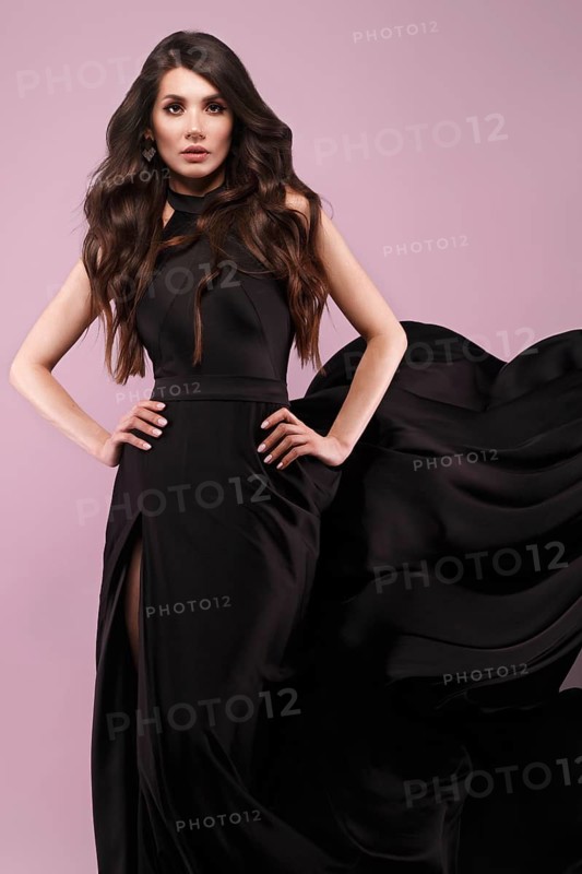 Beautiful brunette woman with curls and classic make-up in a flying black dress. Beauty face. Photo taken in studio