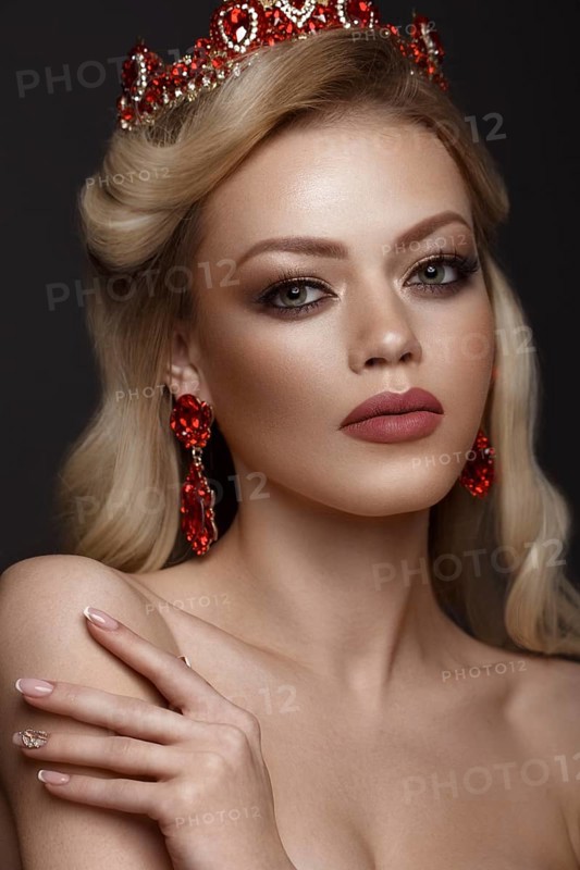 Beautiful blond girl with a golden crown and earrings and professional evening make-up. Beauty face. Picture taken in the studio