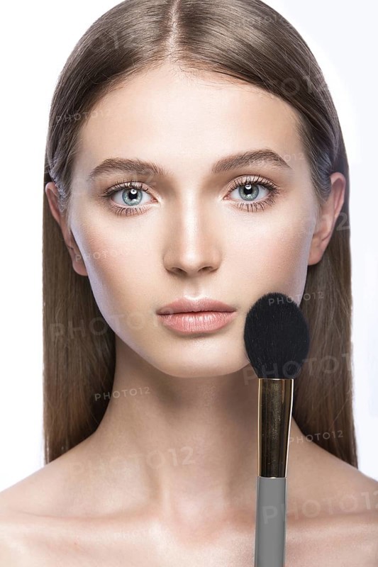 Beautiful young girl with a light natural make-up and beauty tools in hand. Picture taken in the studio on a white background