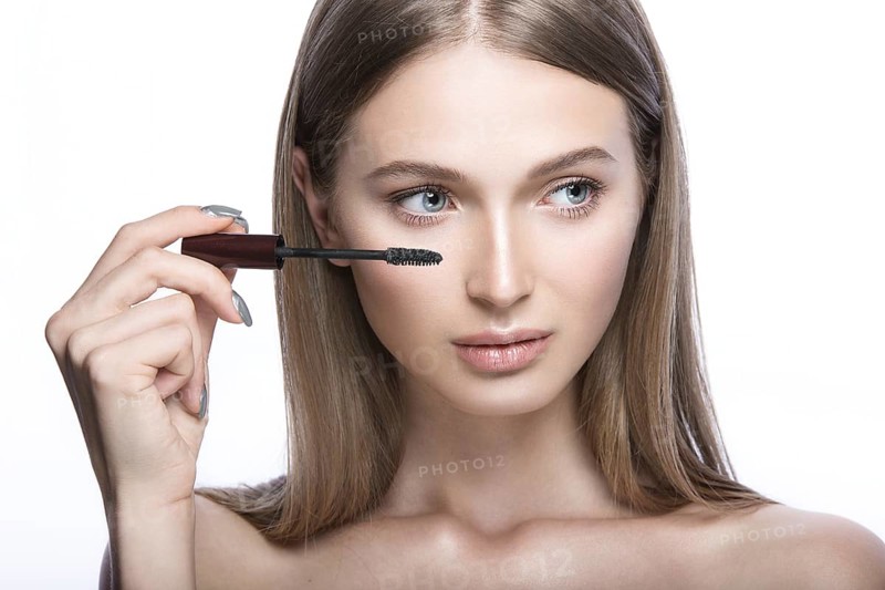 Beautiful young girl with a light natural make-up and beauty tools in hand. Picture taken in the studio on a white background