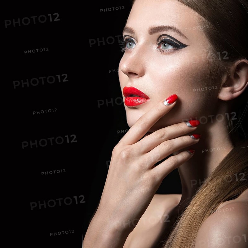 Beautiful young girl with a bright make-up and red nails. Picture taken in the studio on a black background