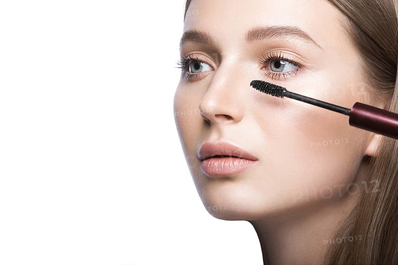 Beautiful young girl with a light natural make-up and beauty tools in hand. Picture taken in the studio on a white background