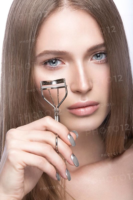 Beautiful young girl with a light natural make-up and beauty tools in hand. Picture taken in the studio on a white background