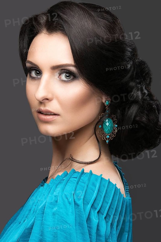 Beautiful girl in a blue dress with evening make-up and hairstyle. Beauty face. Picture taken in the studio on a black background. Hairstyle back view