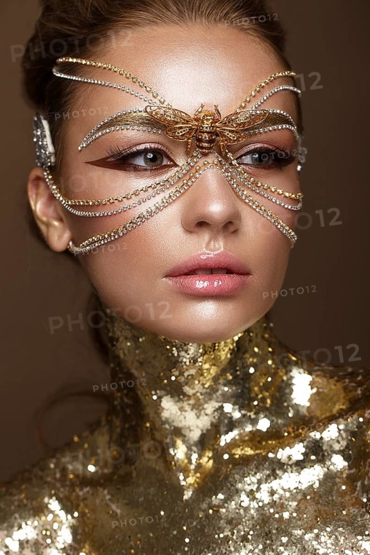 Beautiful girl in a golden mask and bright evening make-up. Beauty face. Photo taken in studio