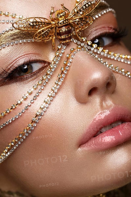 Beautiful girl in a golden mask and bright evening make-up. Beauty face. Photo taken in studio