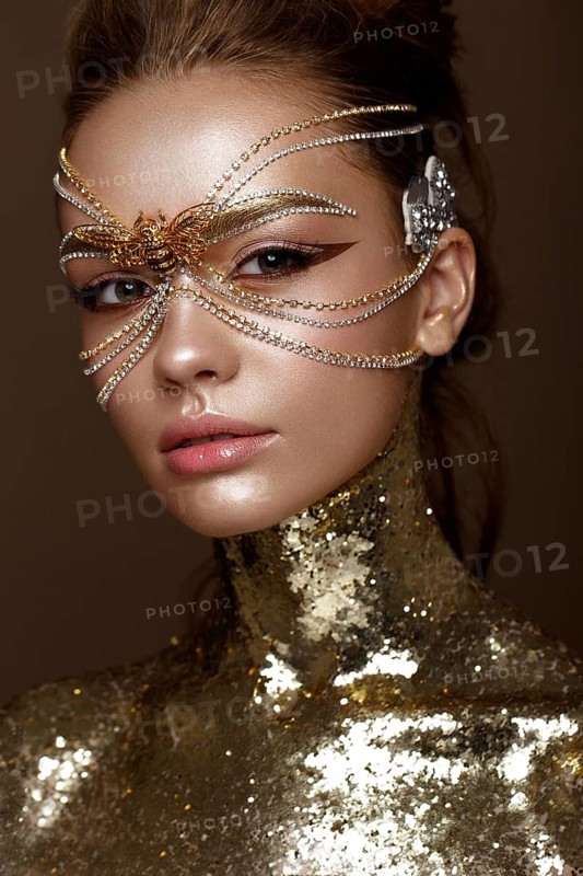 Beautiful girl in a golden mask and bright evening make-up. Beauty face. Photo taken in studio