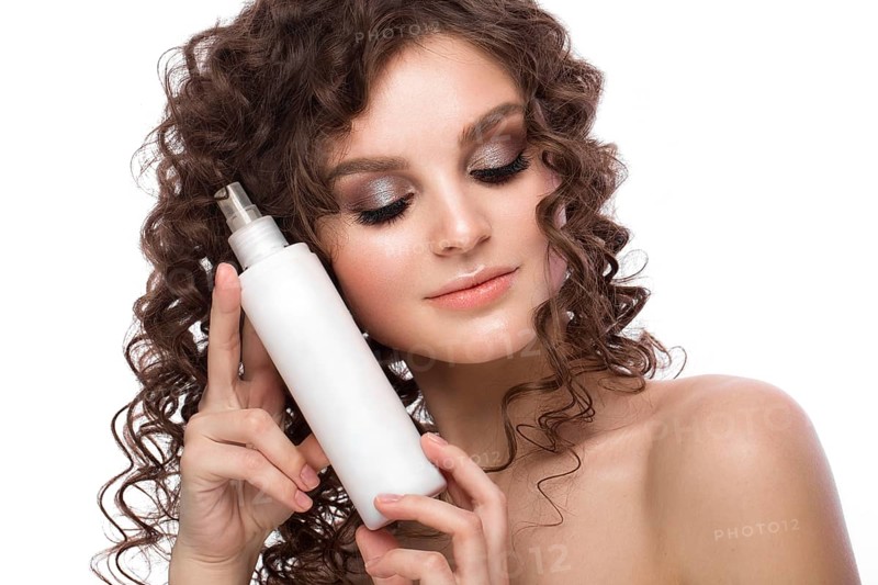 Beautiful brunette girl with a perfectly curly hair with spray bottle